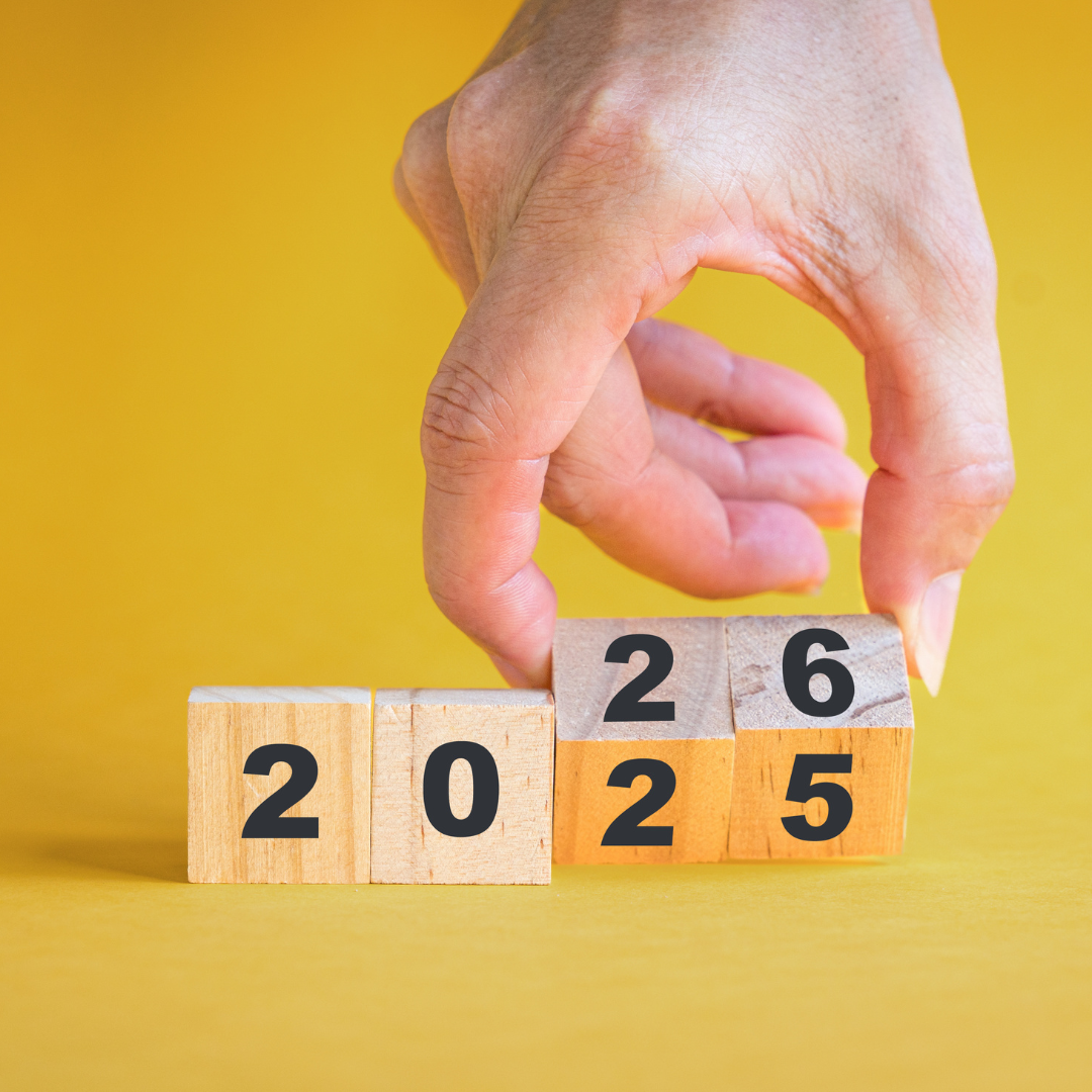 Hand flipping wooden blocks from 2025 to 2026 on a yellow background, symbolizing leaving the past behind and starting fresh in the new year