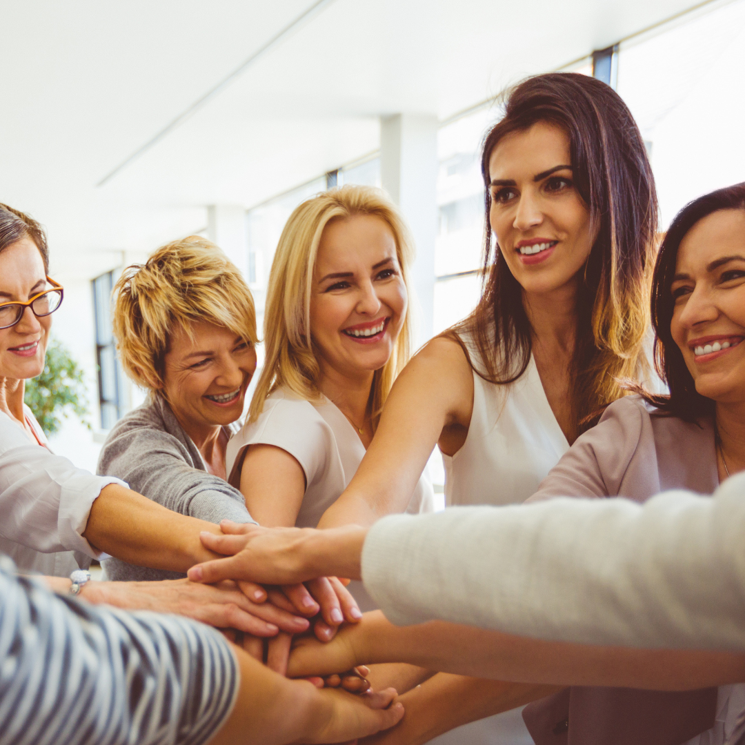 A group of professional women smiling and joining hands in teamwork, symbolising collaboration, unity and shared purpose