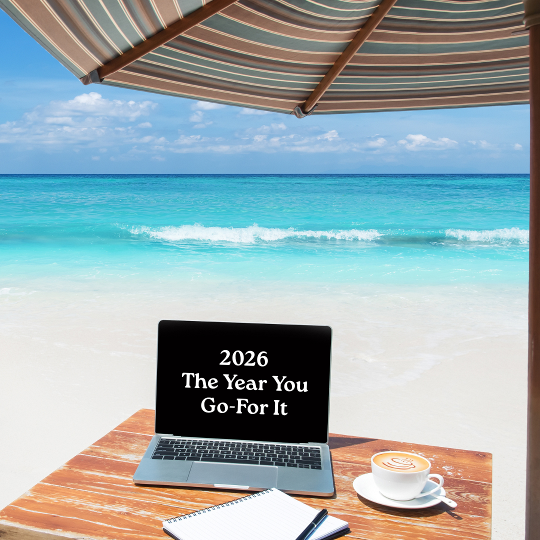 A laptop on a wooden beach table under an umbrella with coffee and a notebook, showing the words “2026 The Year You Go-For It,” symbolizing career freedom and clarity for women leaving corporate life.