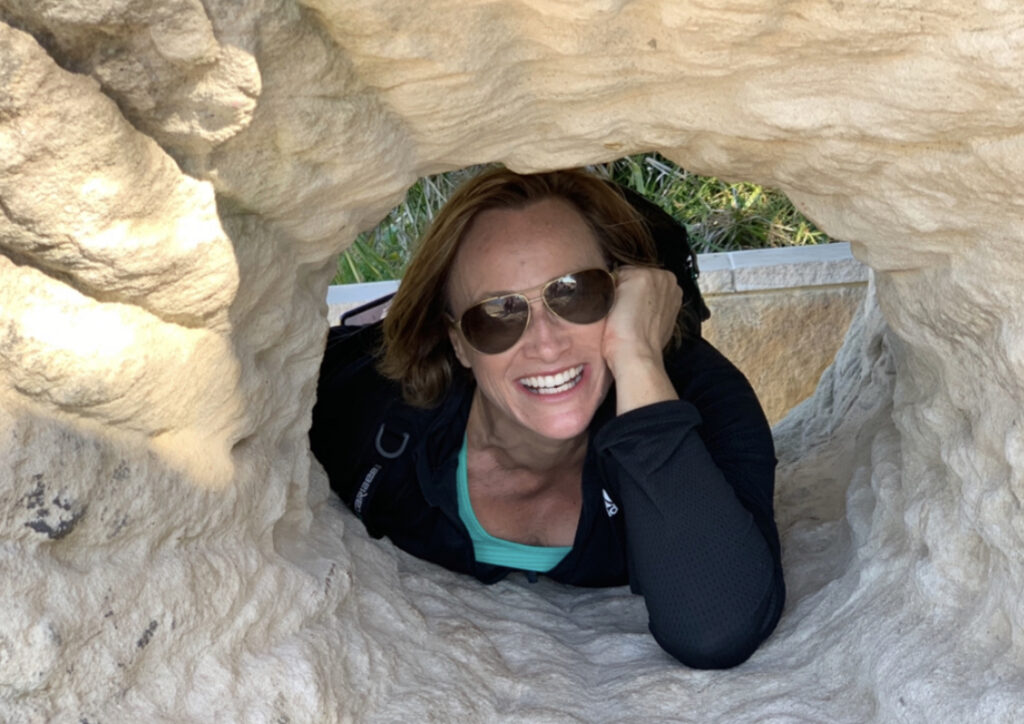 Michelle Crutcher smiling through a rock opening, symbolising freedom and transition out of corporate life.