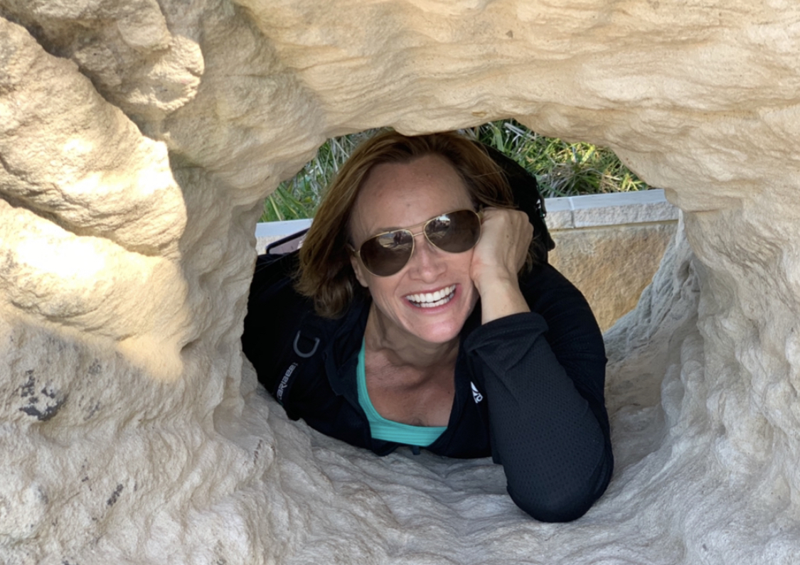 Michelle Crutcher smiling through a rock opening, symbolising freedom and transition out of corporate life.
