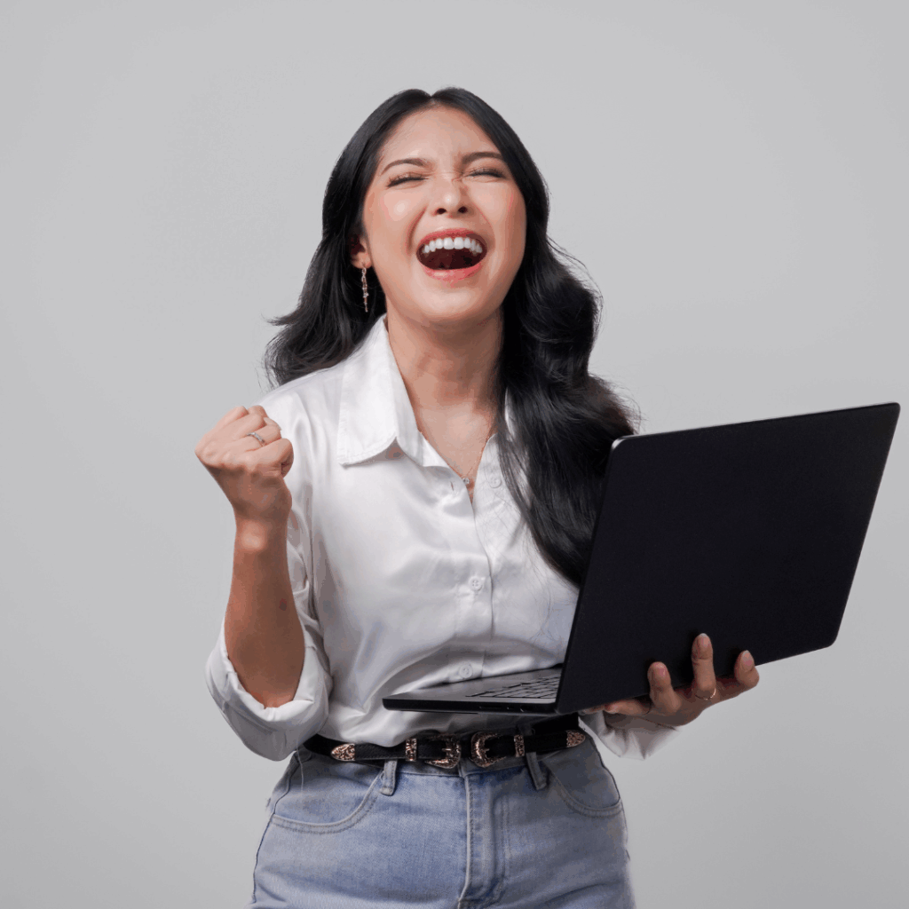 A confident professional woman celebrating with joy while holding a laptop, representing clarity, confidence, and empowerment during her career transition from corporate to entrepreneurship.