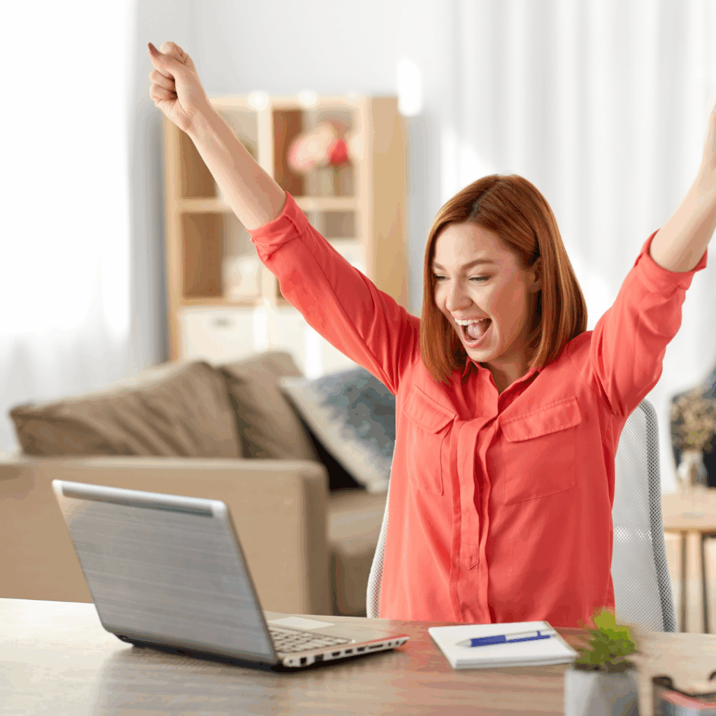 A smiling woman celebrating her first coaching client win while working on her laptop at home.