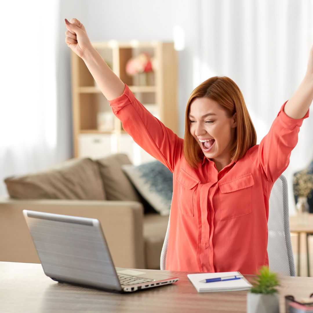 A smiling woman celebrating her first coaching client win while working on her laptop at home.